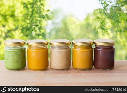 healthy eating, baby food and nutrition concept - vegetable or fruit puree in glass jars on wooden table over green natural background. vegetable or fruit puree or baby food in jars