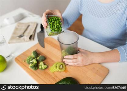 healthy eating, baby food, diet and cooking concept - close up of woman hand adding pea to measuring cup with broccoli. woman hand adding pea to measuring cup