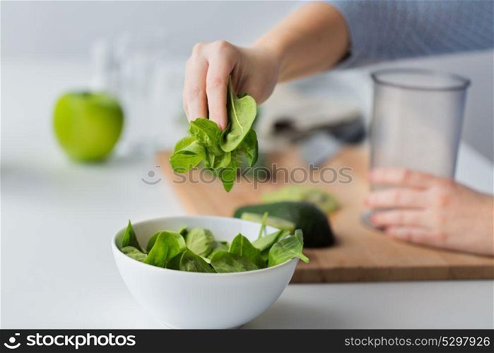 healthy eating, baby food, diet and cooking concept - close up of woman hand adding spinach leaves to bowl. close up of woman hand adding spinach to bowl