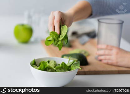 healthy eating, baby food, diet and cooking concept - close up of woman hand adding spinach leaves to bowl. close up of woman hand adding spinach to bowl