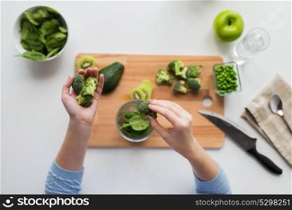 healthy eating, baby food, diet and cooking concept - close up of woman hand adding broccoli to measuring cup with spinach. woman hand adding broccoli to measuring cup