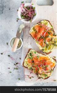 Healthy eating concept. Toast with avocado cream and smoked salmon on the white wooden board. Smoked salmon, cream cheese and pesto toast sandwiches with radish microgreens sprouts. Top view