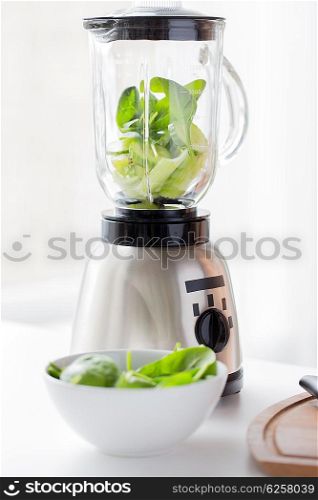 healthy eating, cooking, vegetarian food, detox and diet concept - close up of blender jar and green vegetables on table at home