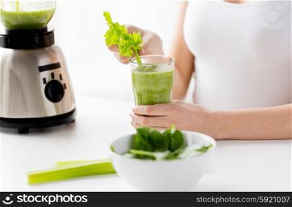 healthy eating, cooking, vegetarian food, diet and people concept - close up of young woman decorating green detox shake or smoothie with celery at home