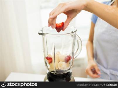 healthy eating, cooking, vegetarian food, diet and people concept - close up of woman with blender making banana strawberry fruit shake at home