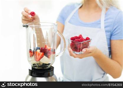 healthy eating, cooking, vegetarian food, diet and people concept - close up of woman with blender making fruit shake at home