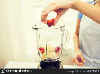 healthy eating, cooking, vegetarian food, diet and people concept - close up of woman with blender making banana strawberry fruit shake at home