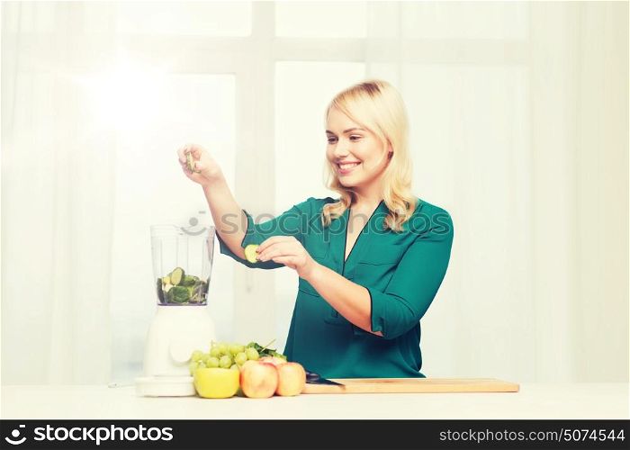 healthy eating, cooking, vegetarian food, diet and people concept - smiling young woman putting fruits and vegetables into blender at home kitchen. smiling woman with blender cooking food at home