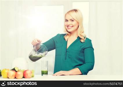 healthy eating, cooking, vegetarian food, diet and people concept - smiling young woman with blender shaker jug pouring green vegetable smoothie or juice into glass at home kitchen. happy woman with blender jug pouring juice at home