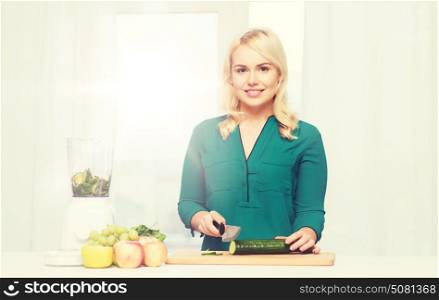 healthy eating, cooking, vegetarian food, diet and people concept - smiling young woman with blender and knife chopping fruits and vegetables on cutting board at home. smiling woman with blender cooking food at home