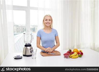 healthy eating, cooking, vegetarian food, diet and people concept - smiling young woman with blender and fruits at home