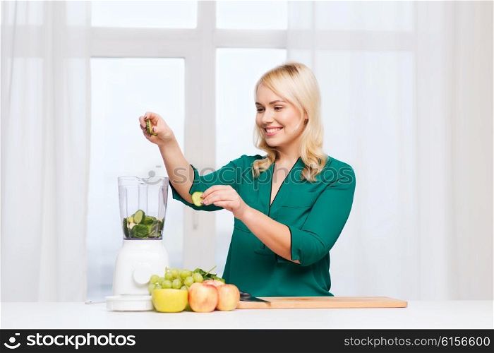 healthy eating, cooking, vegetarian food, diet and people concept - smiling young woman putting fruits and vegetables into blender at home kitchen
