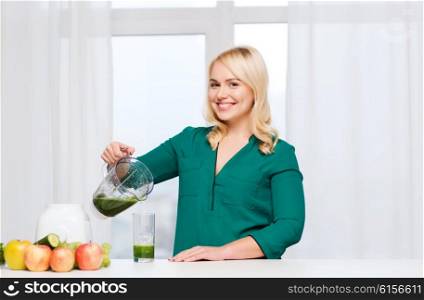 healthy eating, cooking, vegetarian food, diet and people concept - smiling young woman with blender shaker jug pouring green vegetable smoothie or juice into glass at home kitchen