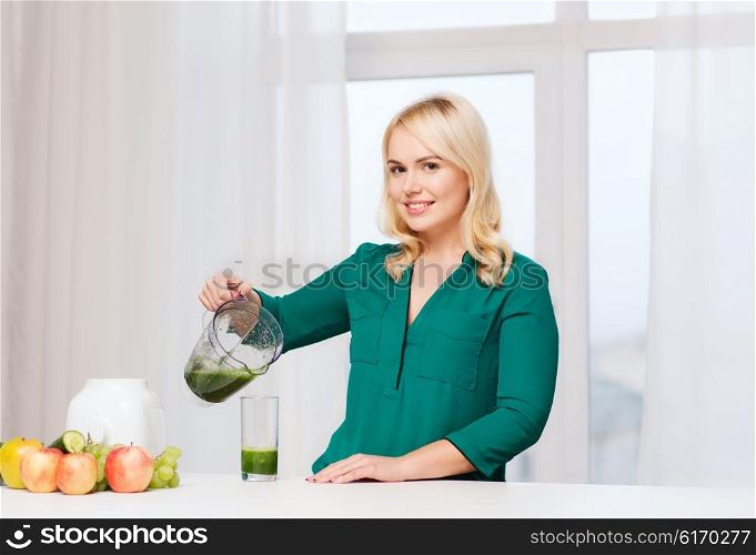 healthy eating, cooking, vegetarian food, diet and people concept - smiling young woman with blender shaker jug pouring green vegetable smoothie or juice into glass at home kitchen