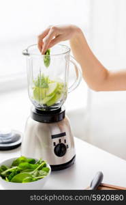 healthy eating, cooking, vegetarian food, dieting and people concept - close up of young woman hand putting green vegetables into blender and making detox shake or smoothie at home