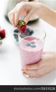 healthy eating, cooking, vegetarian food, dieting and people concept - close up of woman hands decorating milkshake with strawberry at home