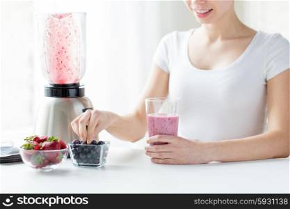 healthy eating, cooking, vegetarian food, dieting and people concept - close up of woman with blender and berries preparing milk shake at home