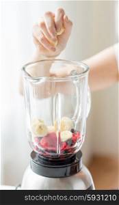 healthy eating, cooking, vegetarian food, dieting and people concept - close up of woman hand with blender adding banana for fruit shake at home