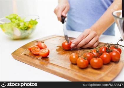 healthy eating, cooking, vegetarian food, dieting and people concept - close up of woman chopping tomatoes with knife on cutting board