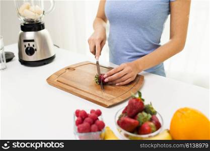 healthy eating, cooking, vegetarian food, dieting and people concept - close up of woman chopping strawberry at home