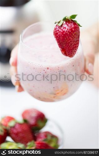 healthy eating, cooking, vegetarian food, dieting and people concept - close up of hand holding glass of fruit strawberry shake at home