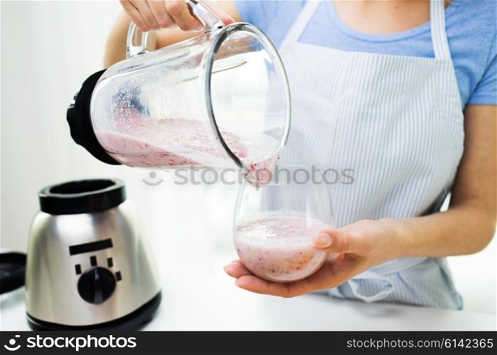 healthy eating, cooking, vegetarian food, dieting and people concept - close up of young woman pouring fruit shake from blender shaker jug to glass at home