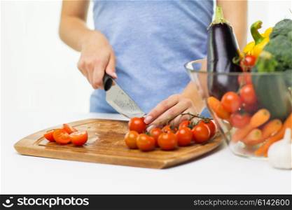 healthy eating, cooking, vegetarian food, dieting and people concept - close up of woman chopping tomatoes with knife on cutting board