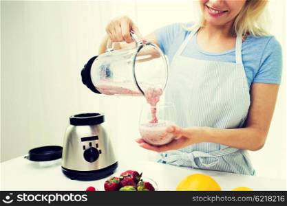 healthy eating, cooking, vegetarian food, dieting and people concept - close up of young woman pouring fruit shake from blender shaker jug to glass at home