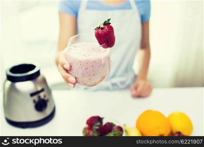 healthy eating, cooking, vegetarian food, dieting and people concept - close up of woman holding glass of fruit strawberry shake at home