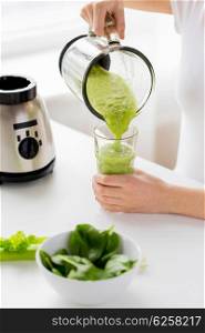 healthy eating, cooking, vegetarian food, dieting and people concept - close up of young woman with green vegetables pouring detox shake or smoothie from blender jar to glass at home
