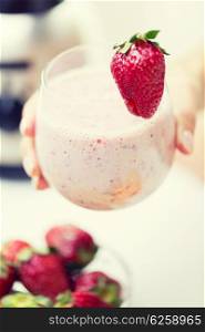 healthy eating, cooking, vegetarian food, dieting and people concept - close up of hand holding glass of fruit strawberry shake at home