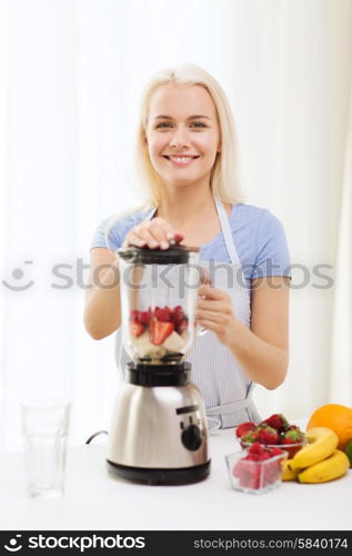 healthy eating, cooking, vegetarian food, dieting and people concept - smiling young woman putting fruits for fruit shake to blender shaker at home