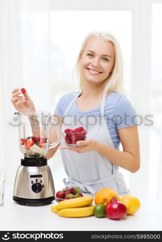 healthy eating, cooking, vegetarian food, dieting and people concept - smiling young woman putting fruits and berries for fruit shake to blender shaker at home