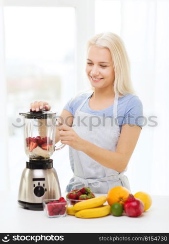 healthy eating, cooking, vegetarian food, dieting and people concept - smiling young woman putting fruits for fruit shake to blender shaker at home