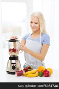 healthy eating, cooking, vegetarian food, dieting and people concept - smiling young woman putting fruits for fruit shake to blender shaker at home