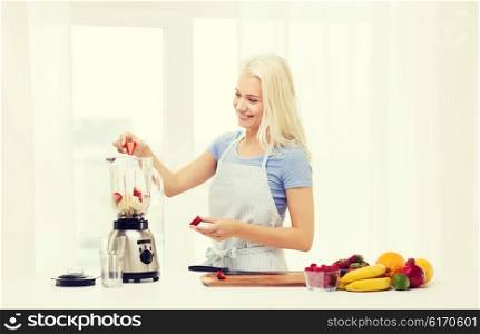 healthy eating, cooking, vegetarian food, dieting and people concept - smiling young woman putting fruits and berries for fruit shake to blender shaker at home