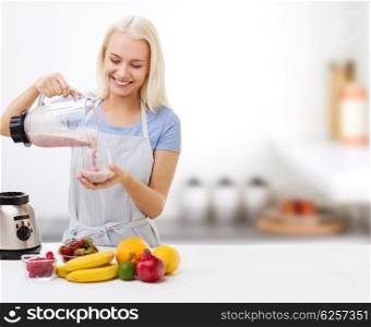 healthy eating, cooking, vegetarian food, dieting and people concept - smiling young woman with blender and fruits pouring milk shake into glass over kitchen background