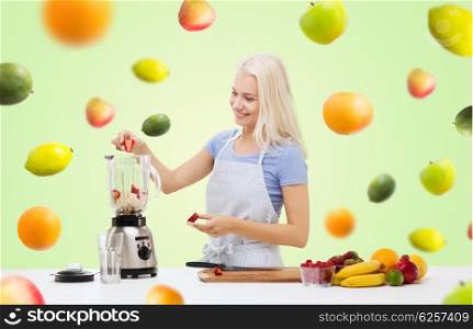 healthy eating, cooking, vegetarian food, dieting and people concept - smiling young woman putting fruits and berries for fruit shake to blender shaker over green background with falling fruits