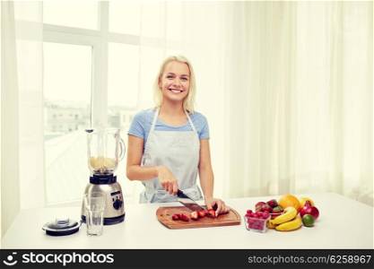 healthy eating, cooking, vegetarian food, dieting and people concept - smiling young woman with blender chopping fruits and berries for fruit shake at home