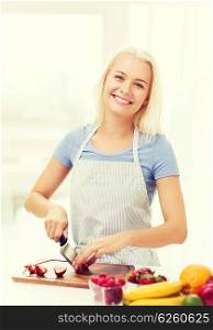 healthy eating, cooking, vegetarian food, dieting and people concept - smiling young woman chopping fruits and berries at home