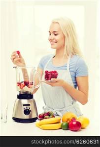 healthy eating, cooking, vegetarian food, dieting and people concept - smiling young woman putting fruits and berries for fruit shake to blender shaker at home
