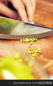 healthy eating, cooking, vegetarian food, kitchenware and people concept - close up of woman chopping green onion with knife on wooden cutting board