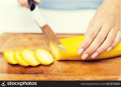 healthy eating, cooking, vegetarian food, vegetable and people concept - close up of woman hands chopping squash with knife on wooden cutting board