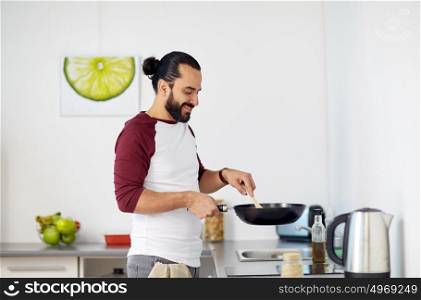 healthy eating, culinary and people concept - happy man with frying pan cooking food at home kitchen. man with frying pan cooking food at home kitchen