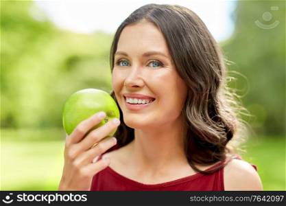 healthy eating, dental and people concept - portrait of happy woman with green apple at summer park. happy woman eating green apple at summer park