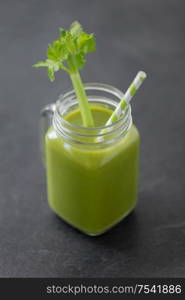 healthy eating, detox and vegetable diet concept - close up of glass mug of green fresh celery juice or smoothie with paper straw on slate stone background. close up of glass mug with green celery juice