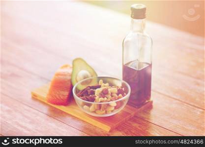 healthy eating, diet and culinary concept - close up of salmon fillets, avocado, olive oil bottle and nuts in glass bowl on table