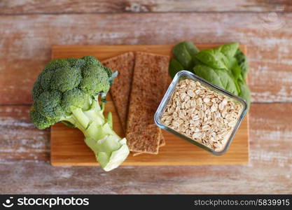 healthy eating, diet and fiber rich in food concept - close up of broccoli, crispbread, oatmeal and spinach on wooden table