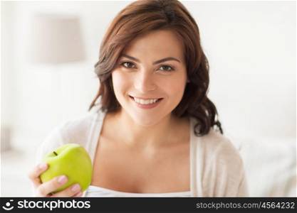 healthy eating, diet and people concept - smiling young woman with green apple at home. smiling young woman eating green apple at home
