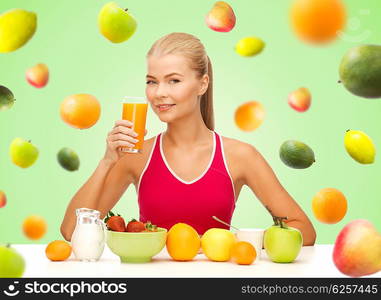 healthy eating, diet, detox and people concept - happy young woman having breakfast and drinking orange juice over green background with falling fruits